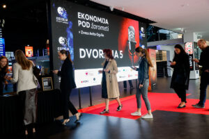 Attendees walk along a red carpet at an event featuring a large screen displaying "Ekonomija pod žarometi" and "Dvorana 5."