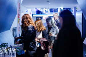 A group of people gather around a beverage station in a modern, dimly lit indoor space.