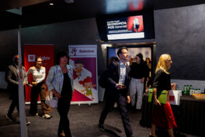 Attendees walk through a conference hall with banners and a screen displaying an event titled "EKONOMIJA POD ZAROMETI."