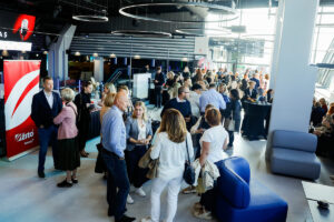 A lively gathering of people in a modern, well-lit event space with circular lighting fixtures and branded signage.